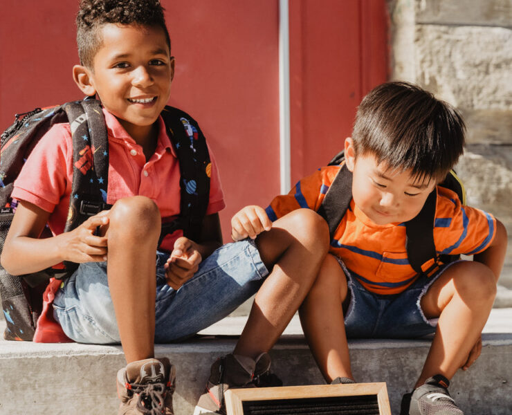 two children sitting on school steps with back to school sign