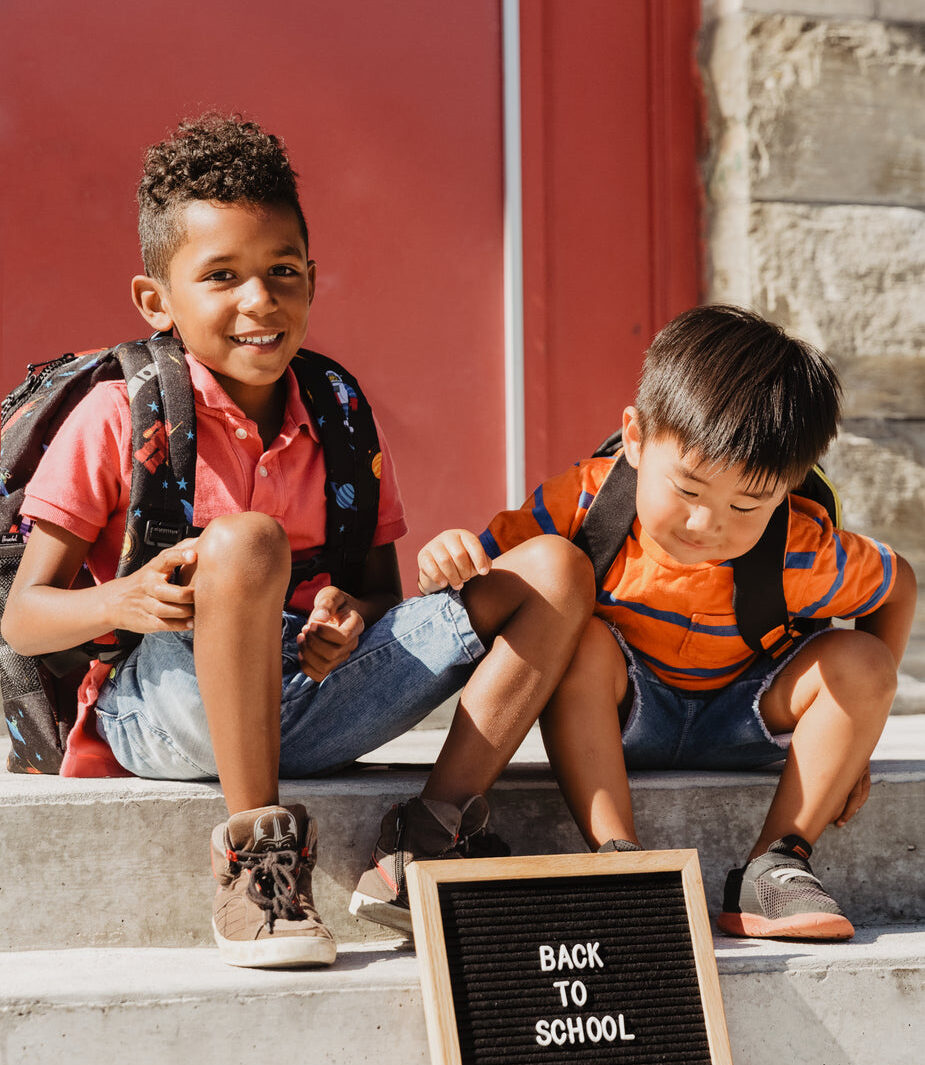 two children sitting on school steps with back to school sign